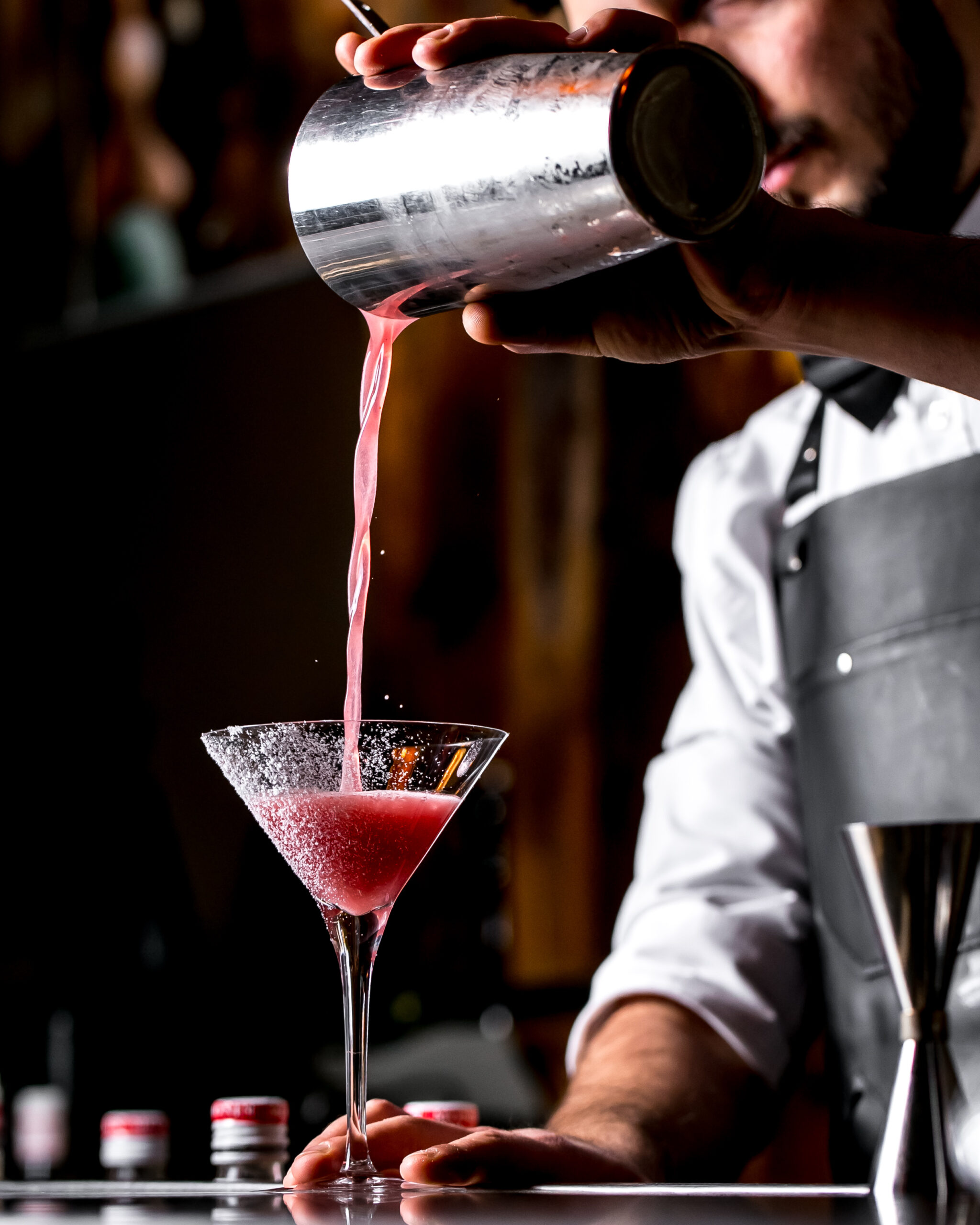 bar tender pours cocktail from cocktail shaker into martini glass